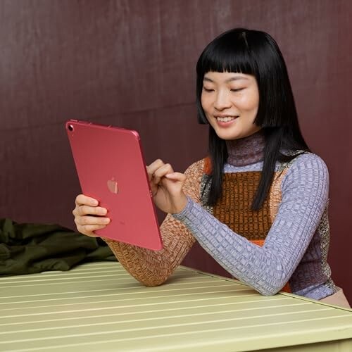 Woman smiling while using a red tablet at a table.